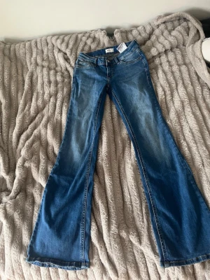 Blå bootcut jeans från Only - Säljer ett par blå bootcut jeans från Only med klassisk femficksdesign och utsvängda ben. Jeansen har en snygg tvätt med ljusare partier framtill och bakfickor. Perfekta för dig som gillar retrovibbar och vill ha ett par jeans med skön passform.midja: 29cm byxa: 76cm