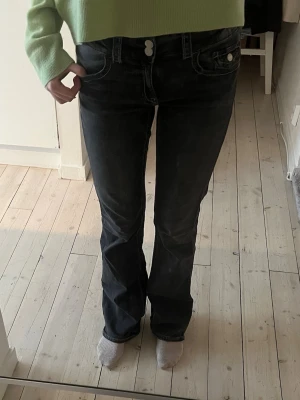 Svarta low waist bootcut jeans  - Säljer ett par svarta low waist bootcut jeans och klassiska fem fickor. Jeansen har en lätt tvättad look och sitter snyggt över höfterna. Materialet är denim och passformen är något utsvängd nedtill. Perfekta för en trendig och avslappnad stil.