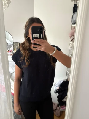 Svart stickad ärmlös tröja - Säljer en svart stickad ärmlös tröja med rund hals och avslappnad passform.