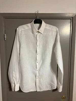 Vit linneskjorta från These glory days - Klassisk vit skjorta i linne från These glory days med lång ärm och knappar framtill. Skjortan har en stilren och tidlös design med normal passform och mjuk känsla, perfekt för en clean och fräsch look. Knappt använd!