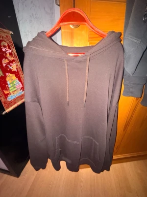 Svart hoodie från YOURTURN - En svart hoodie från YOURTURN med klassisk huva och dragsnören. Hoodien har en stor magficka framtill och avslappnad passform. Perfekt för dig som gillar en enkel och stilren look. Materialet känns mjukt och bekvämt.