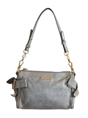 Miu Miu Vitello Lux Axelremsväska  - Snygg grå handväska från Miu Miu i mjukt skinn med guldfärgade metalldetaljer och justerbar axelrem. Väskan har dekorativa rosetter på sidorna och ett diskret Miu Miu-logo framtill. Perfekt storlek för det viktigaste och stängs med dragkedja.