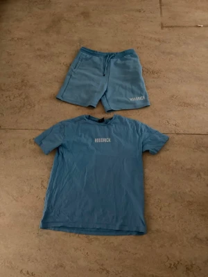 Blått set från Hoodrich - Snyggt blått set från Hoodrich med matchande t-shirt och shorts. Båda plaggen har Hoodrich-loggan tryckt i vitt framtill. T-shirten har rund hals och korta ärmar, medan shortsen har dragsko i midjan och sidofickor. Perfekt för en avslappnad och trendig look.