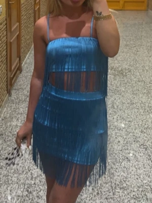 Blå fransklänning med smala axelband - Säljer ett blått sett med fransdetaljer och smala axelband. Settet har en unik design med genomskinliga partier och är perfekt för dig som vill sticka ut. Materialet känns lätt och följsamt.