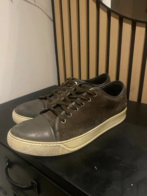 Bruna låga sneakers i mocka och läder - Snygga bruna sneakers med ovandel i mocka och tåparti i slätt läder. Skorna har vita sulor och bruna skosnören. Har sina spår av användning men är fortfarande i fint skick😁