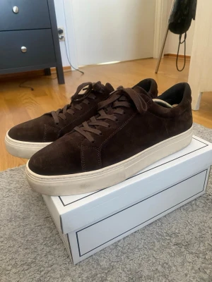 Bruna Vagabond skor med vit sula - Snygga sneakers i mörkbrun mocka med matchande bruna skosnören och en chunky vit sula. Klassisk låg modell som passar till det mesta och ger en clean look. Perfekta för dig som gillar stilrena och tidlösa skor.