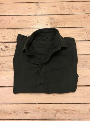 Mörkgrön skjorta från COS - Stilren mörkgrön skjorta från COS med klassisk krage och bröstficka. Skjortan har knäppning framtill och långa ärmar. Perfekt för dig som gillar minimalistisk design och enkel stil.