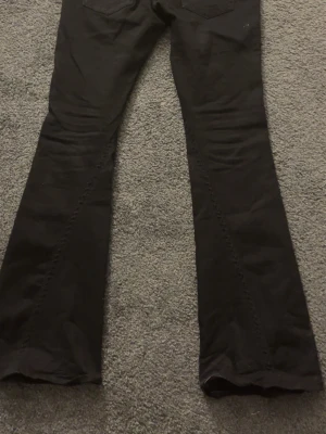 True religion jeans - Säljer ett par svarta jeans med utsvängda ben och klassisk femficksmodell. Jeansen har en snygg söm längs benen som ger extra edge till looken. Perfekta för dig som gillar retrostil och vill sticka ut lite extra. Helt oanvända men säljer de ändå för 800 27/32