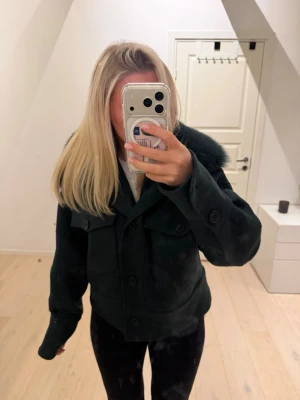Mörkgrön meotine jacka - Säljer en snygg mörkgrön pälsjacka med stor fluffig krage.  Jackan har knappar framtill och två bröstfickor med lock. Perfekt för att hålla sig varm och stilren under kalla dagar.