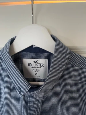 Blå rutig skjorta från Hollister - Säljer en blå rutig skjorta från Hollister i Epic Flex Stretch-material. Skjortan har klassisk krage, bröstficka med logotyp och knappar framtill. Perfekt för dig som gillar en bekväm och stilren look.