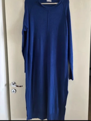 Blå långärmad klänning - En enkel och stilren blå långklänning med långa ärmar och rund halsringning. Klänningen har en rak passform och är tillverkad i ett mjukt material som passar perfekt för både vardag och mer avslappnade tillfällen.