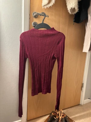 Vinröd ribbad tröja från BikBok - Snygg vinröd ribbad tröja från BikBok med lång ärm och hög hals. Tröjan är figurnära och stretchig, perfekt att styla med jeans eller kjol. Materialet är mjukt och följsamt, vilket gör den superbekväm att bära.