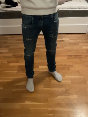 Blå slim fit jeans med slitningar - Säljer ett par blå slim fit jeans med coola slitningar på låren och knäna. Jeansen har klassiska fem fickor och en snygg tvätt som ger en trendig look. Perfekt för dig som gillar en modern och avslappnad stil.