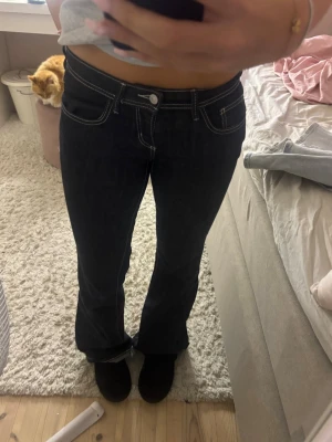 Mörkblå bootcut jeans med vita sömmar - Snygga mörkblå bootcut jeans med tydliga vita kontrastsömmar och låg midja. Klassisk femficksmodell och utsvängda ben. Perfekta för dig som gillar en retroinspirerad look och vill ha jeans som sticker ut lite extra.