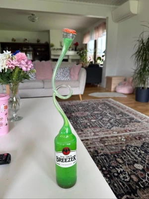Grön Bacardi Breezer flaska med sugrör - En grön Bacardi Breezer flaska med ett långt, snirkligt sugrör i plast. Sugröret är böjt i en spiralform och har en kapsyl på toppen. Perfekt som rolig dekoration eller för att dricka på ett unikt sätt.
