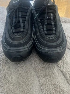 Nike Air Max 97 helsvarta sneakers - Snygga Nike Air Max 97 sneakers i helsvart med ikoniska vågformade detaljer och synlig Air-sula.  Pris kan diskuteras vid snabb affär 