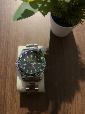 Klocka  - Snygg klocka med rostfritt stålarmband och en grön och svart vridbar bezel. Urtavlan är svart med tydliga index och datumfönster. Klassisk design med robust känsla och lyxig look.