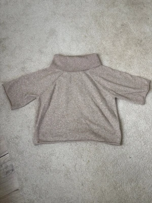 Beige stickad tröja med polokrage - Mysig beige stickad tröja med bred polokrage och halvlånga ärmar. Tröjan har en avslappnad passform och är tillverkad i ett mjukt, melerat material som känns skönt mot huden. 