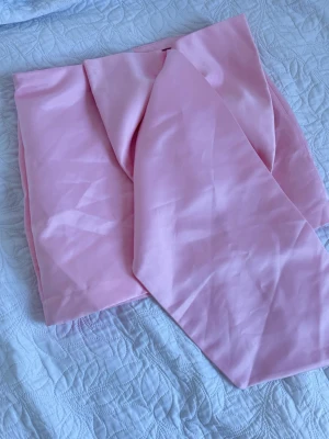 Ljusrosa kjol med rosett  - Aldrig använt. En kortkjol i ljusrosa med glansig material. Kjolen har en rosett framtill och väldigt elegant på. Den är lite insydd. Liten i storleken.