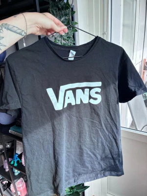 Svart Vans t-shirt med logga - Snygg svart t-shirt med Vanstryck (ej äkta) Klassisk rak passform och rund halsringning. Tillverkad i mjukt bomullsmaterial som är skönt mot huden. Perfekt för dig som gillar streetwear och enkel stil.