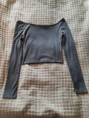 Off shoulder ribbad grå topp - Supersöt ribbad och croppad off shoulder topp från Chiquelle. Den har inbyggda genomskinliga axelband så man slipper oroa sig för att den ska åka ner. Den är storlek S och materialet är polyester och elastan ☀️