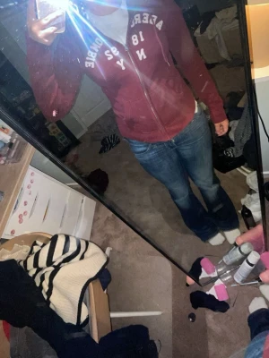 Vinröd hoodie från Abercrombie - Säljer en vinröd hoodie från Abercrombie & Fitch med dragkedja framtill och vit text på bröstet. Hoodien har huva, fickor och långa ärmar. Perfekt för en avslappnad och cool stil.