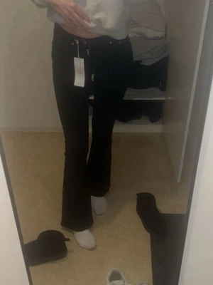 Svarta bootcut jeans med låg midja - Säljer ett par svarta bootcut jeans med låg midja och utsvängda ben. Jeansen har klassisk femficksdesign och dragkedja med knapp framtill. Perfekta för dig som gillar en trendig siluett och vill ha ett par stilrena svarta jeans.