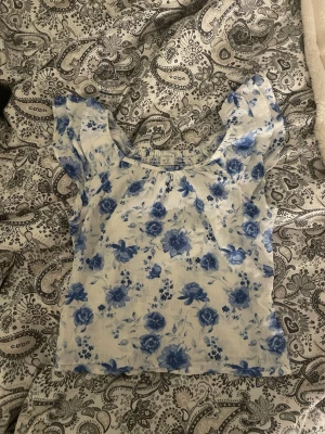 Blommig topp med puffärmar - Söt topp med blått blommönster  och puffiga korta ärmar. Toppen har en smockad rygg och en lätt croppad passform!💗
