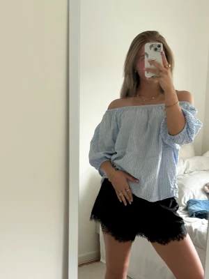 Svarta shorts med spetskant - Säljer en luftig offshoulder topp med blå och vita ränder. Toppen har trekvartsärm och en relaxed fit. Perfekt till sommaren och enkel att stylad med shorts eller kjol.
