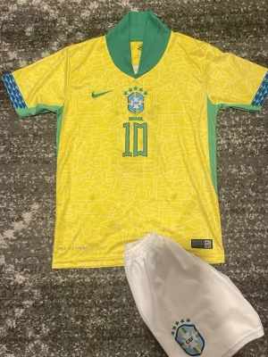 Brasilien matchställ  gul/grön - Säljer ett Brasilien matchställ från Dri-fit med gul tröja, gröna detaljer och nummer 10 och brasilien på bröstet.Neymar jr på ryggen. Tröjan har korta ärmar och klassisk krage. Tillhörande vita shorts med CBF-logga . Perfekt för fotbollsträning eller supporterhäng.okej skick på vänster arm har tråden släpt lite men märka ej av och det finns fläckar som syns på bilden. Storlek 152