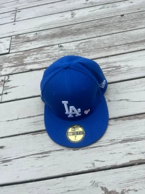 Blå LA Dodgers 59FIFTY keps - Snygg blå fitted keps från New Era med LA Dodgers-logga framtill och broderade detaljer på sidan, inklusive 'Love & Hustle Game' och '1988 World Series'. Klassisk rak skärm och broderad New Era-logga på sidan. Perfekt för dig som gillar streetwear och sportig stil.