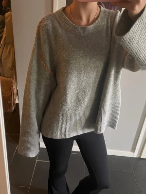 Grå stickad tröja från Gina Tricot - Mysig grå stickad tröja från Gina Tricot. Tröjan har en detalj med orange söm längs axlarna. Använd fåtal gånger. Pris kan diskuteras 💕