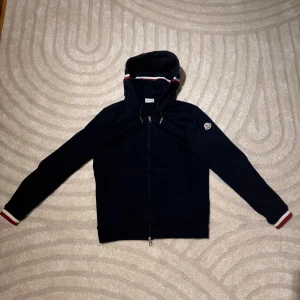 Moncler hoodie  - Snygg mörkblå moncler hoodie med dragkedja och broderad logga på armen. Säljs pga av att den va för liten, endast använd en gång så den är i i nytt skick. Storleken är M 