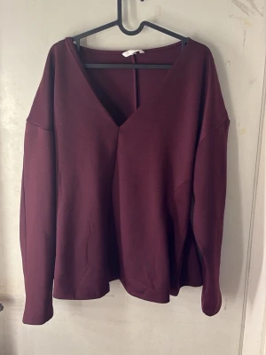 Vinröd v-ringad blus - Snygg vinröd blus med djup v-ringning och lång ärm. Blusen har en avslappnad passform och är tillverkad i ett mjukt, stretchigt material som känns skönt mot huden. Perfekt att styla med jeans eller kjol för en trendig look.