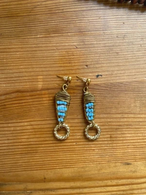 Bohemiska örhängen med turkosa pärlor - Mina handgjorda örhängen.  Vita och blåa pärlor på guldfärgad metalltråd.  Nickelfria!  Följ min Instagram för mer <3 @veras.smycken. Unika örhängen i bohemisk stil med turkosa små pärlor och guldfärgad metalltråd. Örhängena har en spiralformad ring längst ner och en kreativ inslagning av metalltråden runt pärlorna. Perfekta för dig som gillar handgjorda accessoarer med färg.