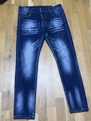 Blå jeans - Snygga blå jeans med tydliga slitningar och tryckdetaljer både fram och bak. Jeansen har raka ben och klassisk femficksmodell. Materialet är denim med en cool tvätt och vita kontrasteffekter. Perfekta för en trendig streetwear-look.