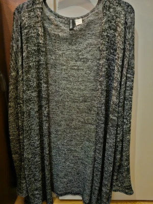 Gråmelerad kofta från H&M Divided - Säljer en lång, öppen gråmelerad kofta från H&M Divided. Koftan har en avslappnad passform och är tillverkad i ett mjukt, stickat material. Perfekt att slänga över en t-shirt eller topp för en chill look.