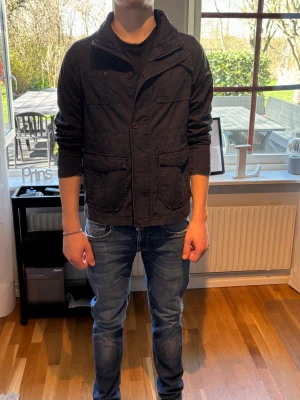 Mörkblå Overshirt/Cardigan - Snygg svart jacka med casual look, stora framfickor och knappar framtill. Jackan har hög krage och är långärmad, perfekt för dig som vill ha en stilren och enkel jacka till vardags. Tillverkad i bomullsmaterial för skön känsla. Är ganska liten i storlek. Dragkedjan är sönder. Men går fortfarande att använda. 