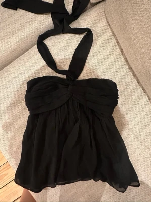Svart halterneck topp från Nelly  - Säljer en svart halterneck topp från Nelly i storlek 32. Den går att knyta på flera sätt och är i ett tunt luftigt material med flera lager