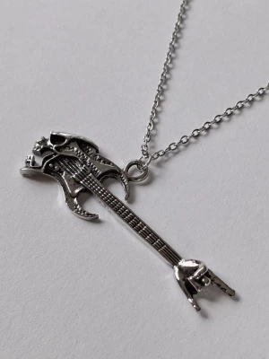 Halsband med elgitarr och dödskalle - halsband i silverfärgad metall med ett coolt hänge format som en elgitarr med dödskalle-detaljer. Perfekt accessoar för dig som gillar rockig stil och vill sticka ut. Kedjan är tunn och smidig, och hänget har många detaljer som ger en edgy vibe. Materialet rostfritt stål. 
