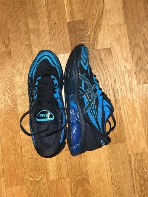 Asics gel 360 - Snygga sneakers från Asics i svart med blå detaljer och mönster. Skorna har en sportig design med klassisk snörning och en rejäl sula i blått och svart. Perfekta för dig som gillar en färgstark och modern look. Dom är äkta
