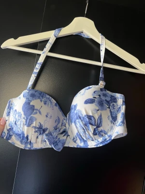 Blåvit blommig bikiniöverdel - Supersnygg bikiniöverdel med blått blommönster på vit botten. Kuporna är vadderade och axelbanden är justerbara för bästa passform. Perfekt för strandhäng eller poolparty. Materialet känns mjukt och följsamt mot huden.