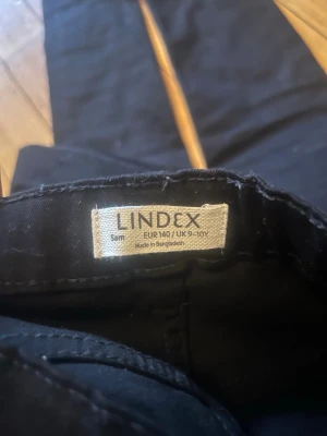 Svarta jeans från Lindex, stl 140 - Svarta jeans från Lindex i storlek 140. Modellen är slim fit med klassisk femficksdesign och normal midja. Perfekta för dig som gillar en enkel och stilren look. Materialet är mjukt och stretchigt för extra komfort.