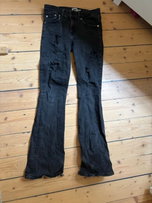 Svarta slitna bootcutlow waist jeans  - Säljer ett par svarta bootcut jeans från 157 med slitningar och hål på benen för en edgy look. Jeansen har låg midja och är tillverkade i stretchigt denimtyg. Perfekta för dig som gillar en avslappnad och trendig stil.