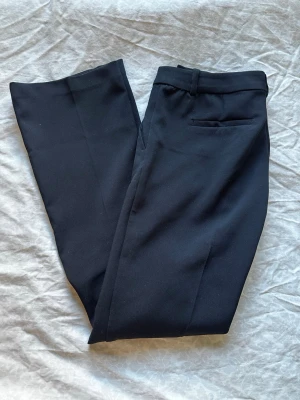 Svarta kostymbyxor från Bik Bok - Snygga svarta kostymbyxor från Bik Bok med klassisk rak passform. Byxorna har en diskret bakficka. Perfekta för en stilren look och tillverkade i ett mjukt tyg som känns bekvämt hela dagen. Knappen vid gylfen har lossnat men det sitter en extra vid tvättrådet så det är bara att sätta dit den nya. Byxorna är i nysskick och ser inte använda ut. Nypris 499, pris kan diskuteras 