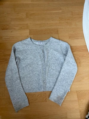 Ljusgrå cropped kofta från Jaime - Ljusgrå kofta med rund hals och knappar framtill från Jaime. Det stod att det var one size i butiken, jag har XS/S i storlek och passar mig.