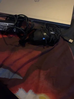 HP bärbar dator med tillbehör - Säljer en silverfärgad HP laptop med klassisk design. Datorn är tillverkad i plast och metall och kommer med laddare och en svart USB-mus. Perfekt för studier eller gaming. HP-loggan syns på locket och undersidan har flera ventilationsgaller.