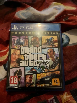 Grand Theft Auto V Premium Edition PS4 - Grand Theft Auto V Premium Edition till PlayStation 4. Omslaget har en färgstark collage-design med olika karaktärer, fordon och actionfyllda scener. Spelet är känt för sin öppna värld och möjligheten att utforska Los Santos. Fodralet är blått och gjort av plast.