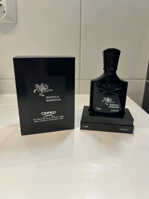 Creed Absolu Aventus parfym 75ml - Lyxig parfym från Creed, modellen Absolu Aventus. Flaskan är svart med silverdetaljer och rymmer 75 ml. Kommer i en elegant svart kartong med matchande design. Perfekt för dig som gillar exklusiva dofter och snygg design.