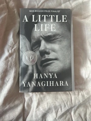A Little Life av Hanya Yanagihara - Säljer romanen 'A Little Life' av Hanya Yanagihara. Boken är på engelska, har ett svartvitt omslag med text och foto, och är en hyllad New York Times bestseller. Perfekt för dig som gillar gripande och djupa berättelser om vänskap och livets utmaningar.